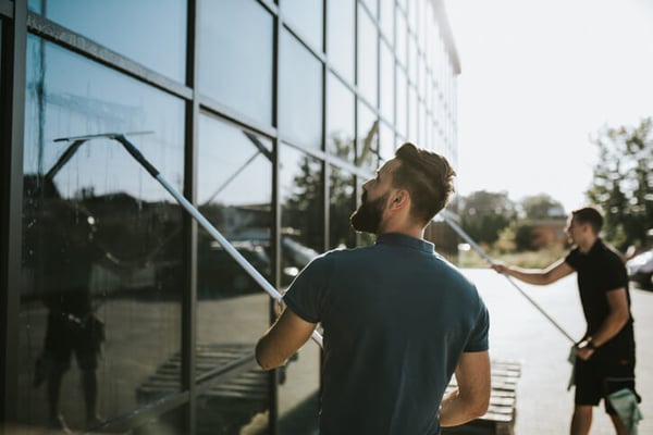 Two professional window cleaners working on cleaning exterior windows of a commercial building.