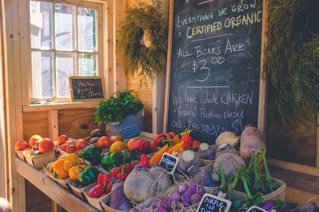 A local grocer's display of certified organic produce including peppers, beets, and herbs.