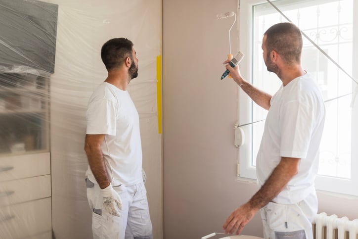 Two paint contractors dressed in all white painting a room in a house.