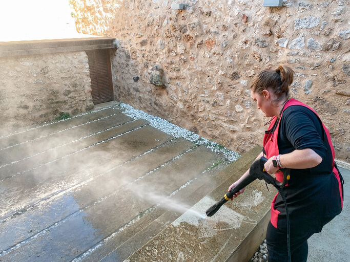 Woman pressure washing concrete in a backyard on a job.