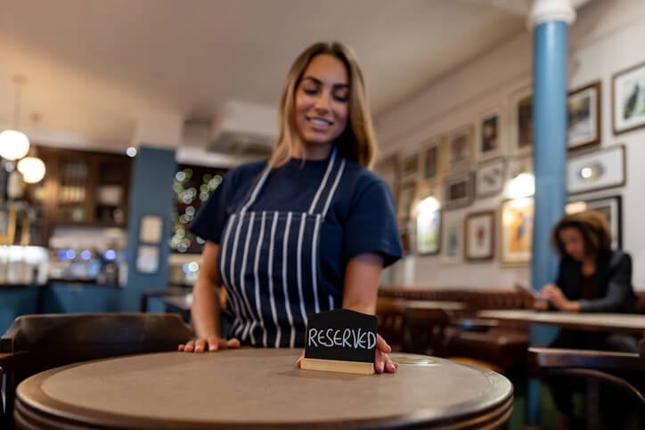Restaurant worker places a reserved sign on a round table.