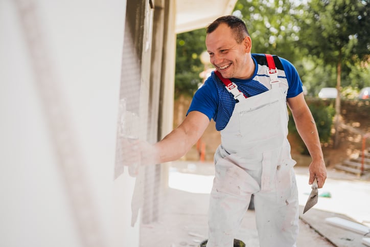A paint contractor wearing white overalls working on a house exterior.
