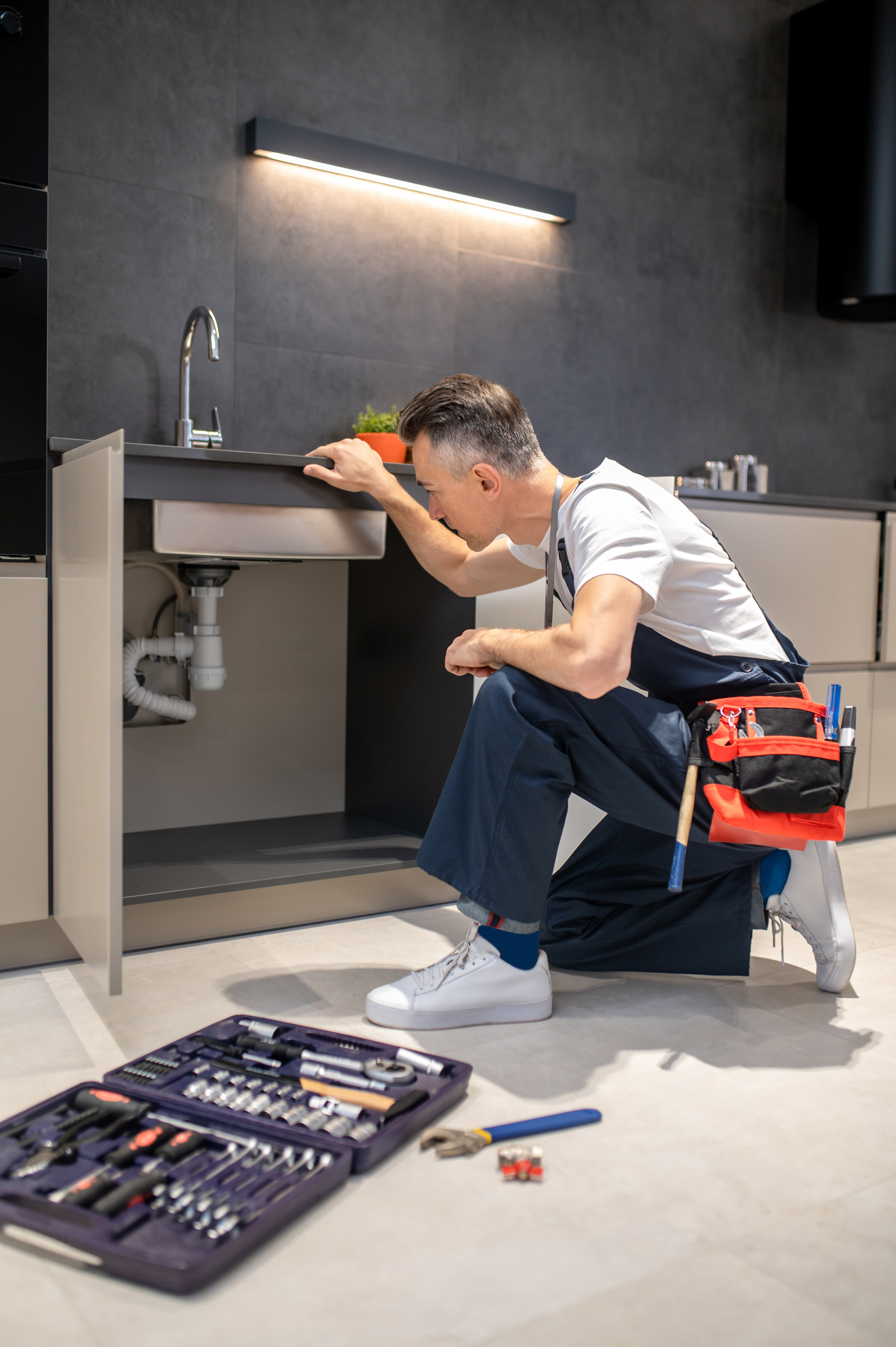 man-kneeling-down-touching-sink-inspecting-pipes